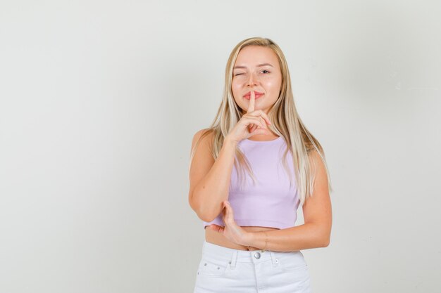 Mulher jovem em camiseta com minissaia mostrando gesto de silêncio com olhos piscando