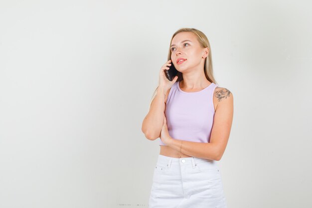 Mulher jovem em camiseta e minissaia falando ao telefone enquanto olha para cima