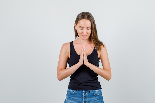 Mulher jovem em camiseta e shorts, mantendo as mãos em gesto de oração e parecendo em paz