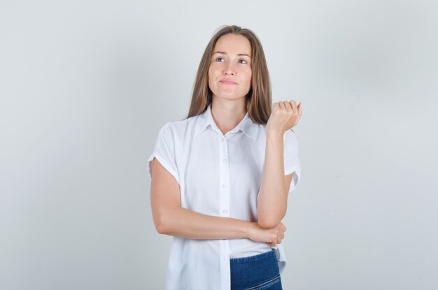 Mulher jovem em camiseta, jeans olhando para cima enquanto pensa e parece alegre