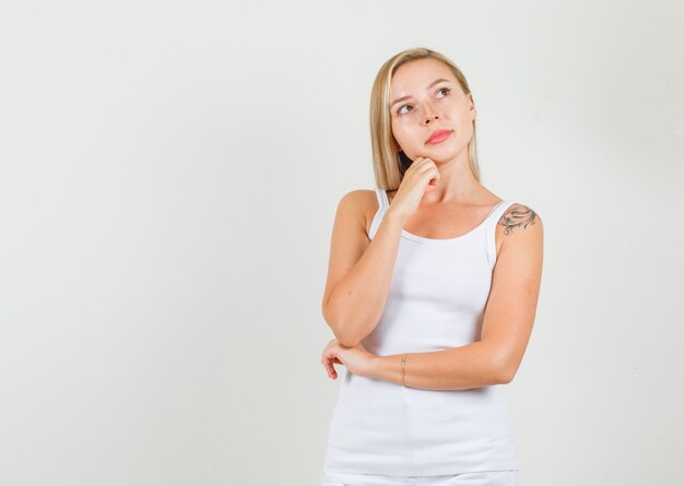 Mulher jovem em camiseta, minissaia pensando enquanto apoia o queixo com o punho