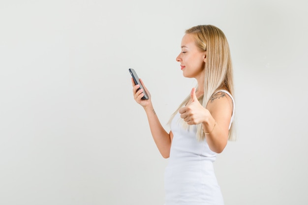 Mulher jovem em camiseta mostrando o polegar enquanto segura um smartphone