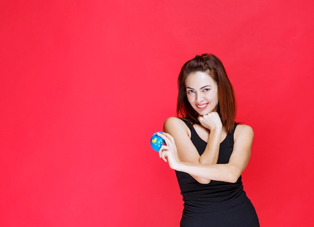 Mulher jovem em camiseta preta segurando um mini-globo mundial