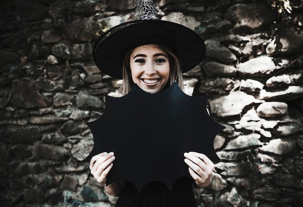 Foto grátis mulher jovem, em, chapéu bruxa, segurando, decoração halloween, e, sorrindo