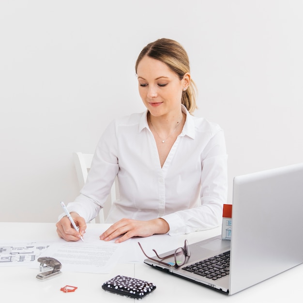 Mulher jovem, em, escritório, fazendo, paperwork, frente, laptop