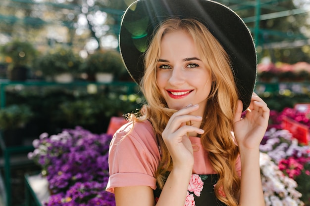 Mulher jovem em êxtase com olhos claros, se passando perto de flores. Linda mulher europeia com chapéu relaxando na laranjeira.