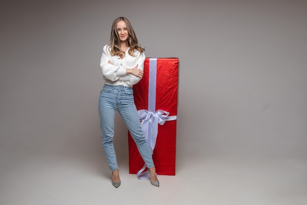 Mulher jovem em forma com grande presente vermelho no fundo cinza do estúdio com espaço de cópia para publicidade de férias