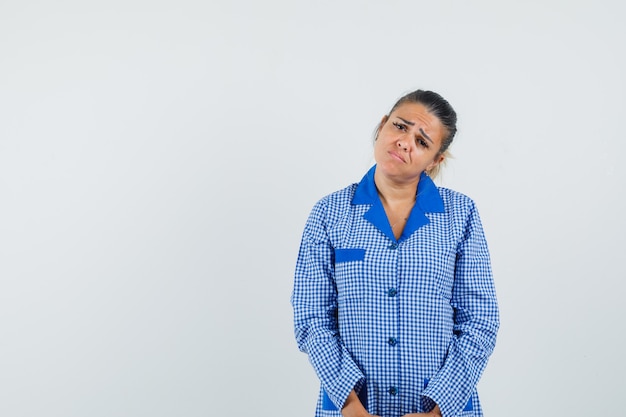 Mulher jovem em linha reta e posando para a câmera com camisa de pijama azul guingão e parecendo lúgubre. vista frontal.