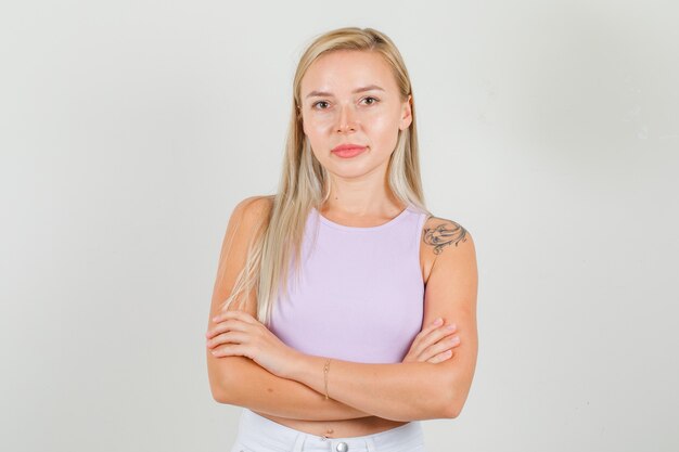 Mulher jovem em pé com os braços cruzados em camiseta, minissaia e parecendo confiante.