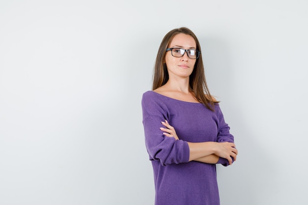 Mulher jovem em pé com os braços cruzados na camisa violeta e parecendo confiante. vista frontal.