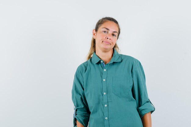 Mulher jovem em pé e posando na frente com uma blusa verde e parecendo uma fofa