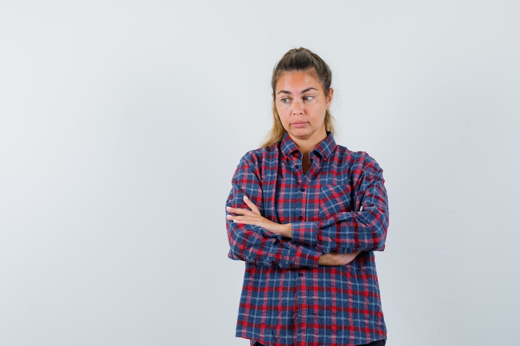 Foto grátis mulher jovem em pé, olhando para o lado e posando para a frente com uma camisa xadrez e parecendo pensativa