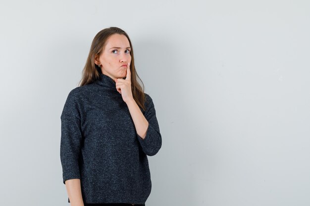 Mulher jovem em pose pensativa com uma camisa e parecendo hesitante