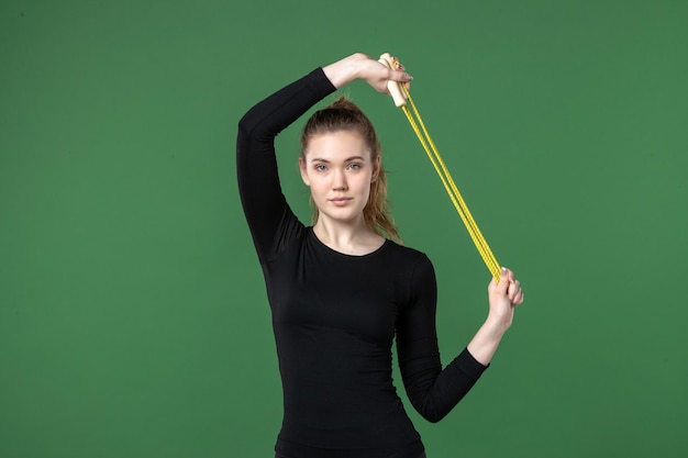 Foto grátis mulher jovem em roupas esportivas pretas, segurando a corda de pular no fundo verde, mulher jovem, de frente, esporte, ioga, saúde, corpo, mulher