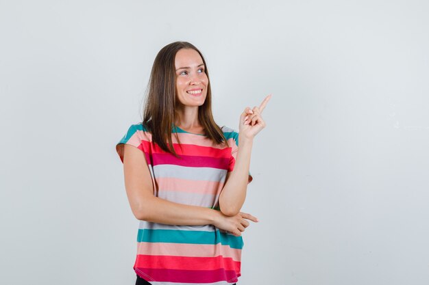 Mulher jovem em t-shirt, calças apontando para cima e olhando alegre, vista frontal.