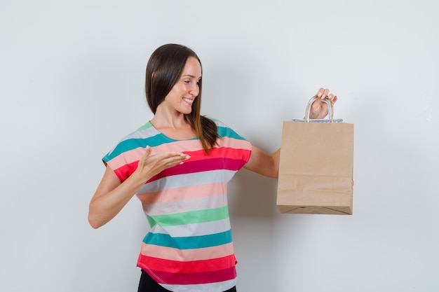 Foto grátis mulher jovem em t-shirt, calças mostrando sacos de papel e parecendo feliz, vista frontal.