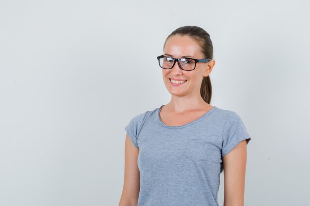 Mulher jovem em t-shirt cinza, óculos e parecendo alegre. vista frontal.