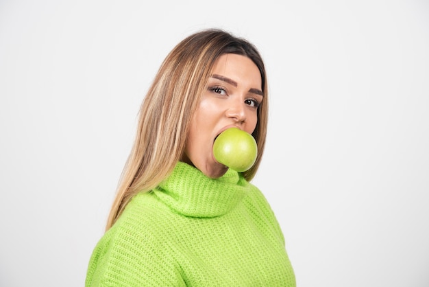 Mulher jovem em t-shirt verde comendo uma maçã.