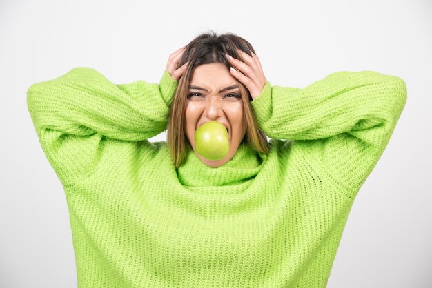 Mulher jovem em t-shirt verde comendo uma maçã.