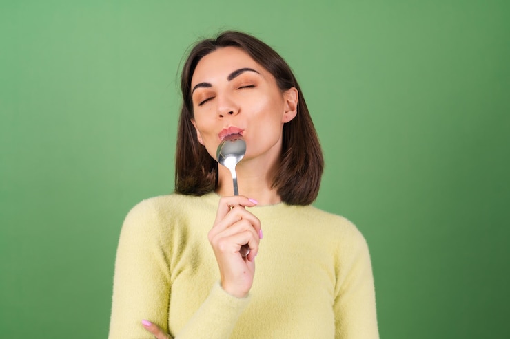 Foto grátis mulher jovem em verde com um suéter amarelo com apetite comendo de uma colher de sopa, desfrutando