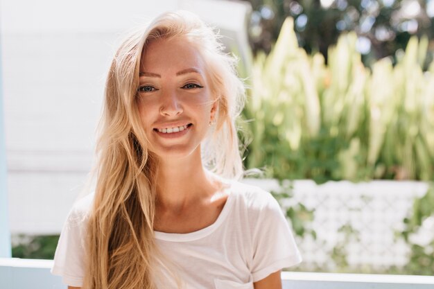 Mulher jovem encantadora usa roupas brancas posando. Modelo feminino bronzeado bonito sorrindo por causa do bom humor.