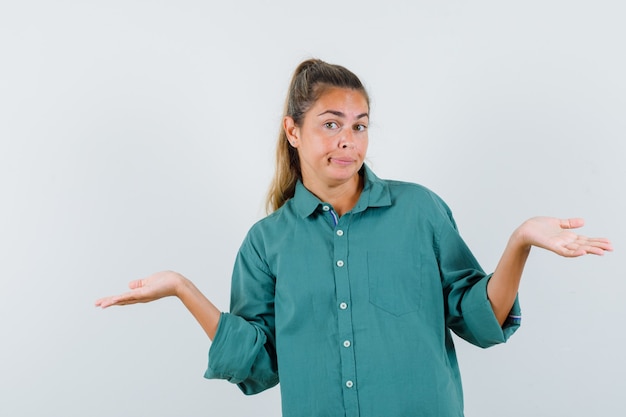 Mulher jovem encolhendo os ombros com uma blusa verde e parecendo confusa