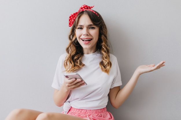 Mulher jovem engraçada com roupa casual, posando no quarto dela com o telefone. romântica garota branca segurando o smartphone na mão.