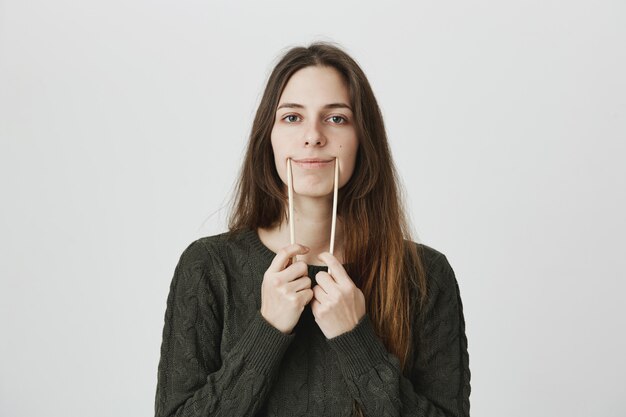 Mulher jovem engraçada fazendo sorriso com shopticks sobre os lábios, brincar