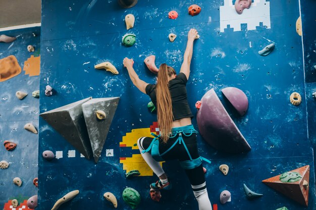 Mulher jovem, escalando, um, alto, indoor, parede artificial, escalada