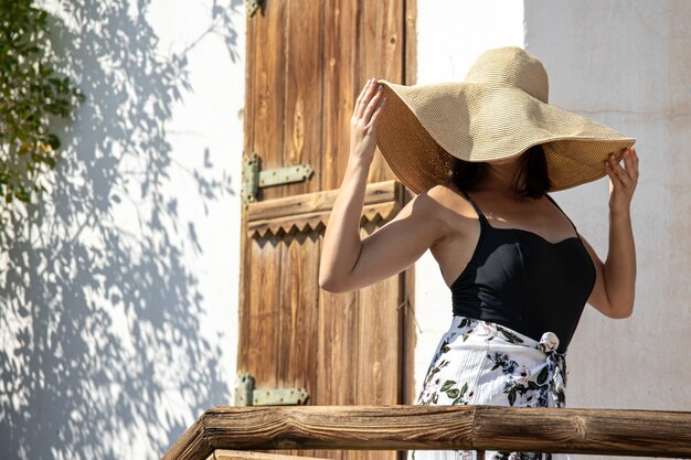 Mulher jovem esconde o rosto dos raios de sol sob um grande chapéu de palha