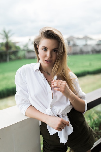 Mulher jovem está de pé na varanda e olhando para a frente. Uma mulher esguia está descansando no terraço.