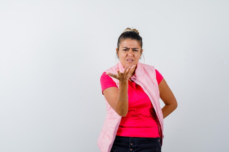 Foto grátis mulher jovem esticando a mão de maneira questionadora, mantendo uma mão na cintura em uma camiseta e jaqueta rosa e parecendo perplexa