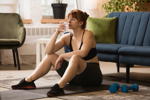 Mulher jovem fazendo exercícios de ioga aeróbica em casa estilo de vida esportivo ficando ativa durante o confinamento