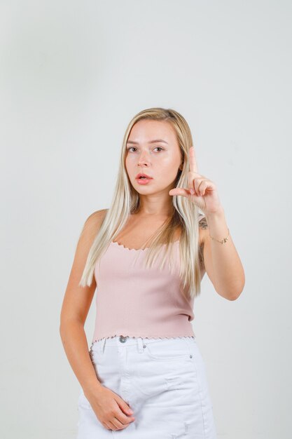 Mulher jovem fazendo sinal de tamanho pequeno em camiseta, minissaia e olhando séria