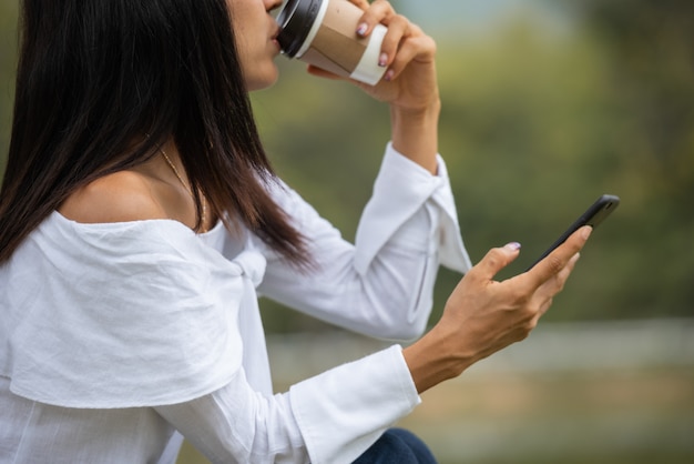 Mulher jovem feliz beber café e usando smartphone