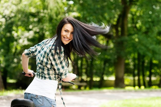 Mulher jovem feliz com bicicleta no parque