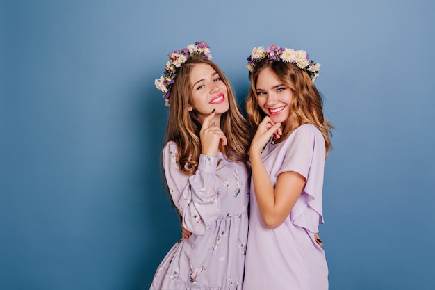 Mulher jovem feliz com cabelo escuro e brilhante tocando seu rosto durante a sessão de fotos com a irmã