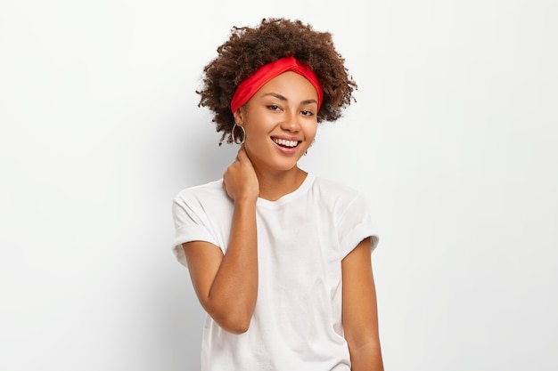 Mulher jovem feliz com cabelos cacheados, tocando o pescoço, curtindo um momento agradável da vida, vestida com roupas casuais