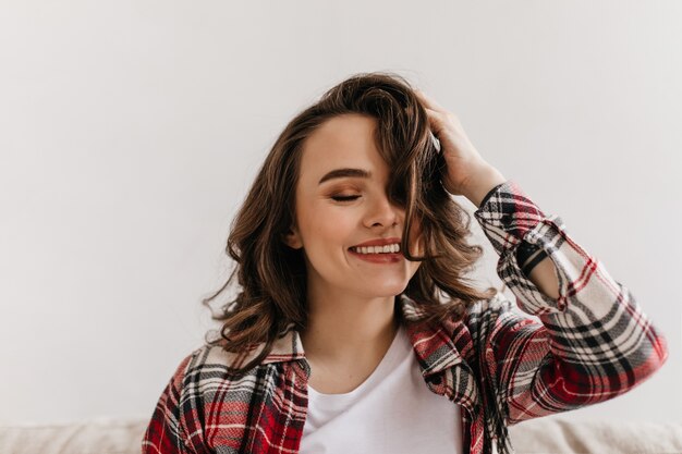 Mulher jovem feliz com camisa xadrez sorri e brinca com o cabelo