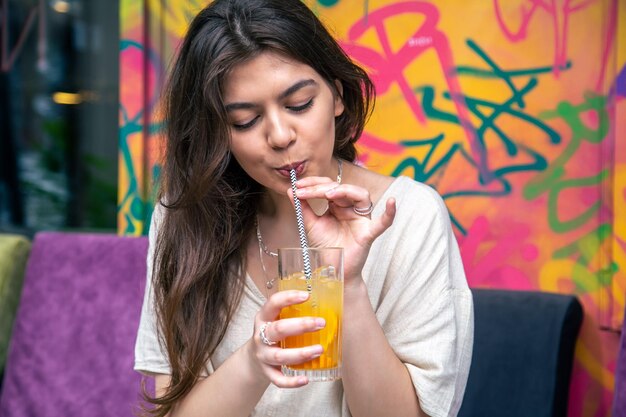 Mulher jovem feliz com um copo de limonada contra uma parede pintada brilhante