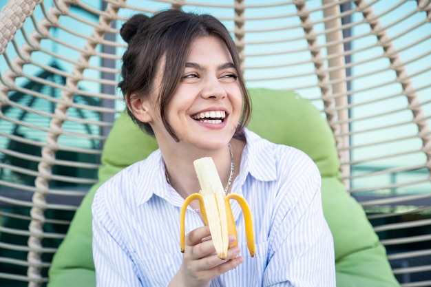 Mulher jovem feliz comendo uma banana enquanto está sentado em uma rede