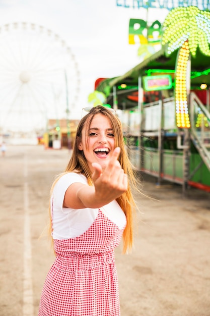 Mulher jovem feliz, convidando alguém com uma mão no parque de diversões