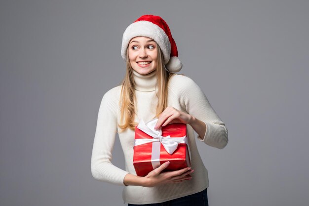 Mulher jovem feliz e animada com chapéu de Papai Noel com caixa de presente isolada na parede cinza