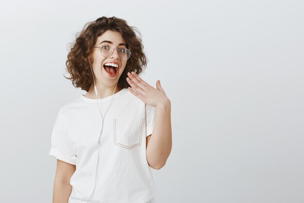 Mulher jovem feliz e extrovertida rindo e sorrindo com os dentes brancos, ouvindo música em fones de ouvido e usando fones de ouvido para se comunicar