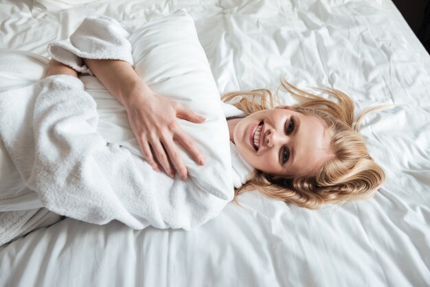 Mulher jovem feliz em roupão deitada na cama