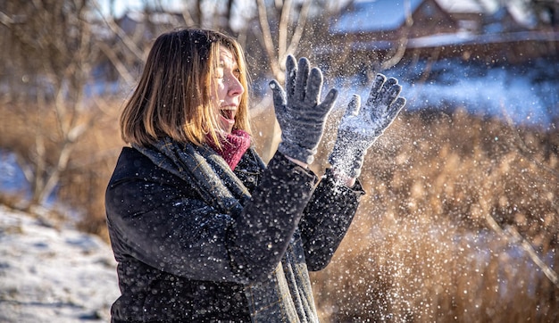 Mulher jovem feliz em uma caminhada no inverno com neve nas mãos