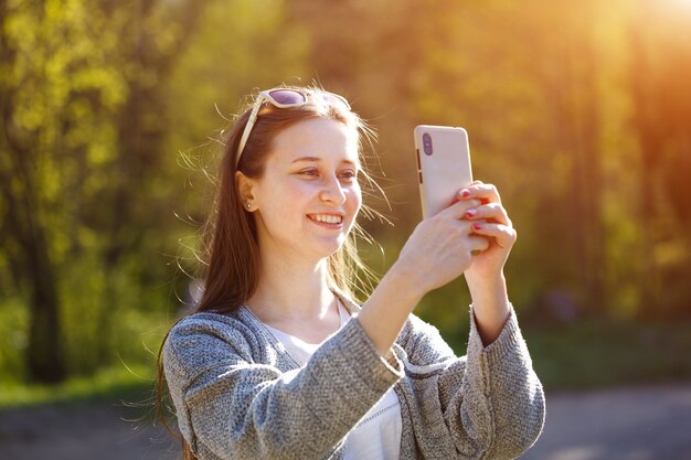 Mulher jovem feliz falando em uma conexão online em seu smartphone. Ao ar livre em um dia ensolarado de primavera no parque