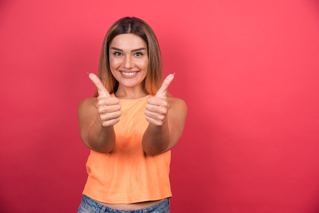 Foto grátis mulher jovem feliz fazendo polegares para cima na parede vermelha.
