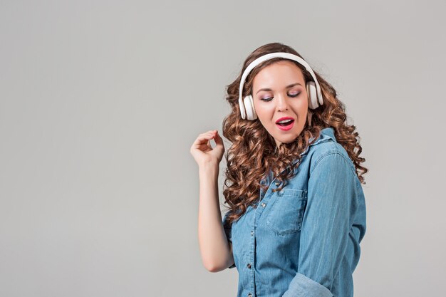 Mulher jovem feliz ouvindo música com fones de ouvido. Retrato isolado em parede cinza