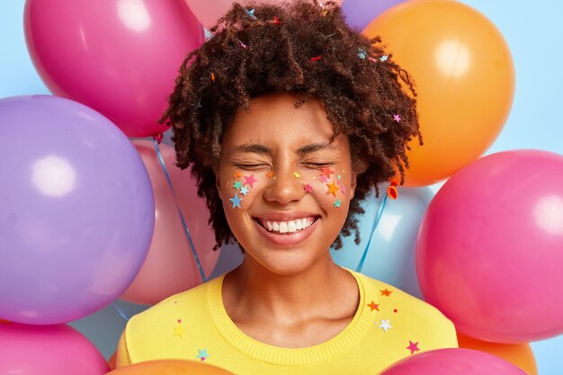 Mulher jovem feliz posando rodeada de balões coloridos de aniversário